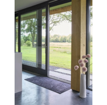 Rechthoekige deurmat met bladmotief voor een moderne glazen schuifdeur met uitzicht op de tuin en een decoratieve vaas.