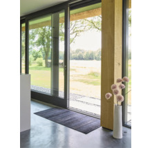 Donkere rechthoekige deurmat op een gepolijste betonnen vloer voor een grote glazen schuifdeur in een licht, modern interieur.