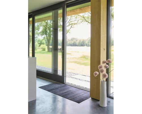 Donkere rechthoekige deurmat op een gepolijste betonnen vloer voor een grote glazen schuifdeur in een licht, modern interieur.