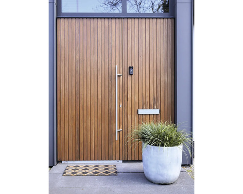 Moderne voordeur met verticale houten latten, bovenlicht, lange metalen handgreep, brievenbus, videodeurbel, plantenbak en deurmat.