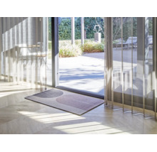 Moderne deurmat met geometrisch boogpatroon op een lichte houten vloer voor een glazen terrasdeur met transparante gordijnen.
