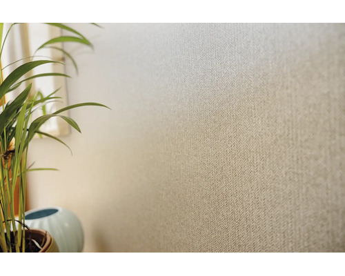 Behang met fijn visgraatmotief en textielook op een muur, naast een kamerplant.