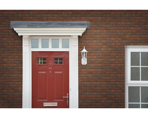 Entree van een woning met een rode voordeur, een wit deurkozijn en een wandlamp aan een bakstenen gevel.
