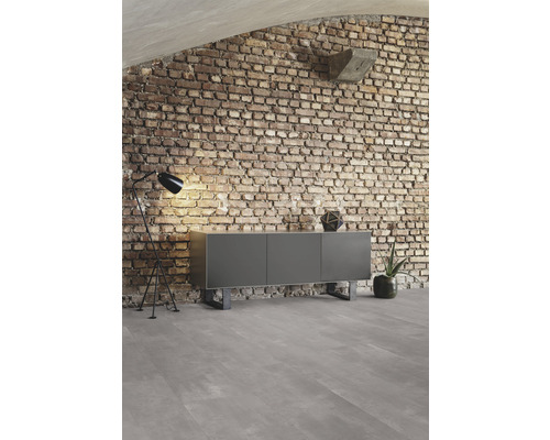 Woonkamer met dressoir, staande lamp en bakstenen muur