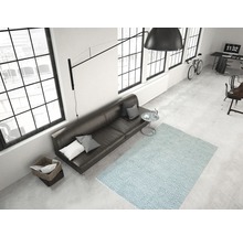 Lichte woonkamer met bank, vloerkleed met geometrisch patroon, lamp en ramen
