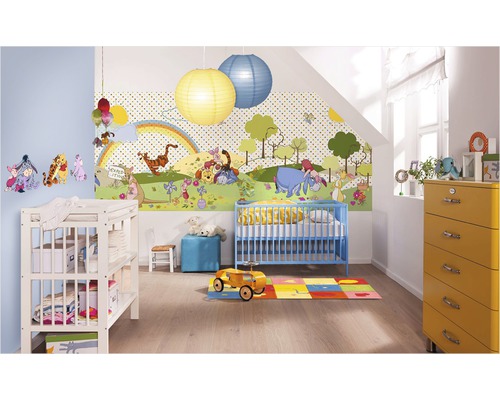 Een kinderkamer met een Winnie de Poeh-behang, een blauw kinderbed, een commode en een gele ladekast.