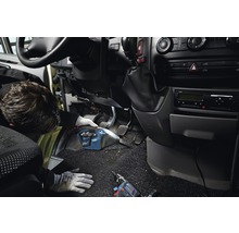 Ambachtsman reinigt voertuiginterieur met snoerloze handstofzuiger. Accuboorschroevendraaier ligt op het tapijt.