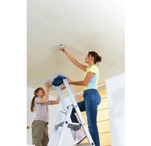 Vrouw op een ladder die een lamp aan een houten plafond bevestigt, met een kind dat helpt