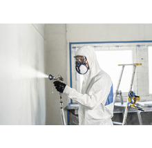 Man met beschermend pak, veiligheidsbril en masker spuit een muur met een verfspuitpistool