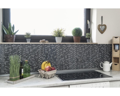 Keukenscène met mozaïektegels, vensterbank met planten, fruitmand en kookplaat.