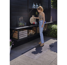 Scene met een buitenruimte met houten planken, decoraties en een vrouw die een snijplank vasthoudt.