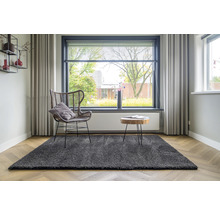 Woonkamer met grijs vloerkleed, fauteuil, houten tafel en raam