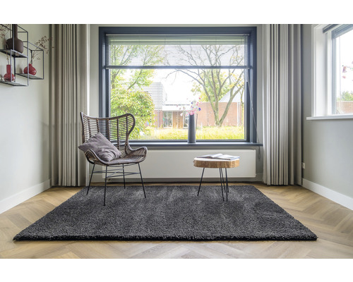 Woonkamer met grijs vloerkleed, fauteuil, houten tafel en raam