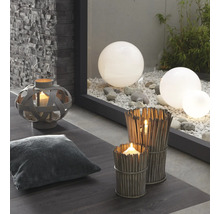 Decoratieve scène met lantaarn, kussen, windlichten van takken en tuinkogels op grind