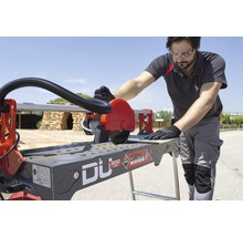 Een man bedient een Rubi tegelsnijmachine om tegels te snijden.