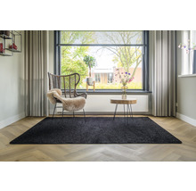 Woonkamer met zwart tapijt, rotan stoel en houten tafel