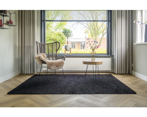Woonkamer met zwart tapijt, rotan stoel en houten tafel