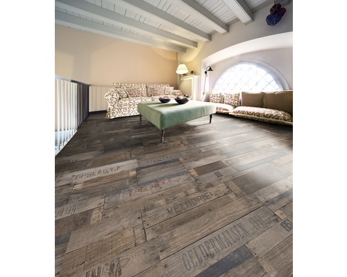 Woonkamer met houten vloer in plankmotief met opschriften, bank en tafel.
