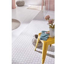 Badkamer met witte, zeshoekige vloertegels, gele kruk, handdoek en badkameraccessoires.
