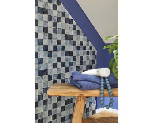 Badkamerwand met mozaïektegels in verschillende blauwtinten, handdoek en decoratie op een houten kruk.