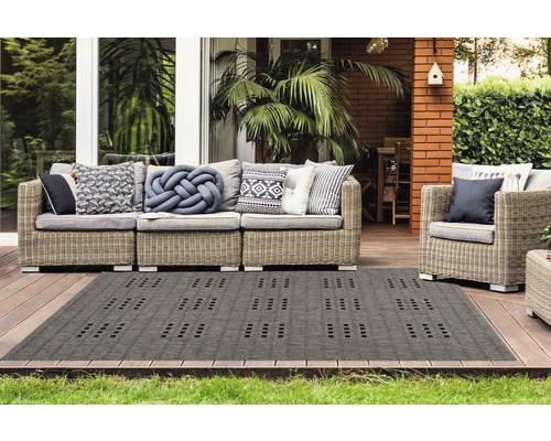 Terras met rotan bank, fauteuil en een grijs buitentapijt met motief.