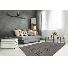 Moderne woonkamer met grijze bank, sierkussens, houten kistenmeubels en een tapijt met patroon