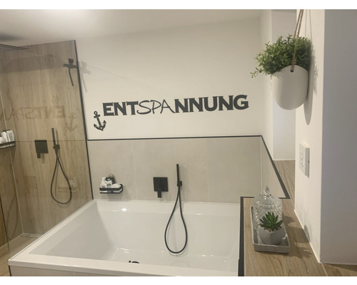 Badkamer met bad, douche, wanddecoratie met het opschrift Ontspanning en een plant