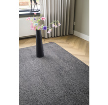 Grijs vloerkleed in woonkamer met een vaas met bloemen op het vloerkleed.