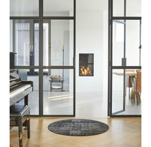 Woonkamer met glazen schuifdeuren, open haard, piano en rond vloerkleed op houten vloer.