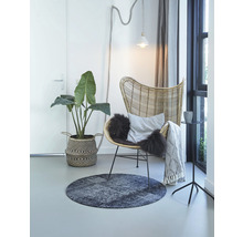 Woonkamer met rotan stoel, rond tapijt, kamerplant en decoratie