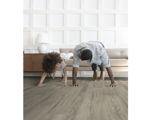 Vader en kind doen yoga op een grijze houten vloer in een lichte kamer.