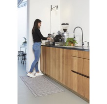 Vrouw bereidt koffie in een lichte keuken met een keukentapijt