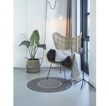 Woonkamer met rotan stoel, rond tapijt met mandala motief en kamerplant in mand