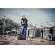 Bouwvakker mengt materiaal in een emmer met een roerder op een bouwplaats.