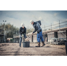 Twee bouwvakkers werken met een schop en mortelmixer op een bouwplaats.