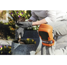 Persoon met kniebeschermers en tuinhandschoenen plant bloemen in een pot