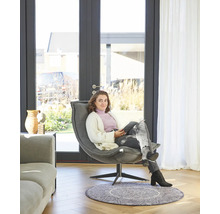 Een vrouw zit in een stoel voor een terrasdeur in een lichte kamer.
