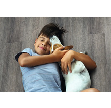 Een jongen ligt met een hond op een laminaatvloer.
