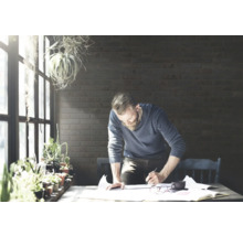 Man met baard werkt aan project aan tafel met planten en documenten.