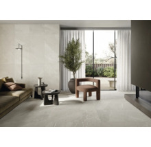 Lichte woonkamer met tegelvloer, bank, fauteuil, kamerplant en daglicht.