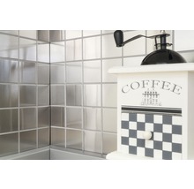 Vierkante metalen tegels aan de wand met een decoratieve koffiemolen