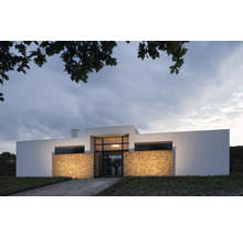 Modern huis met natuurstenen gevel en grote ramen.