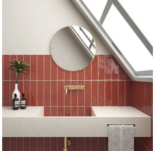Moderne badkamer met rode tegels, ronde spiegel en opzetwastafel.