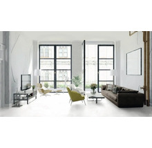 Lichte woonkamer met bank, fauteuils, televisie en grote ramen.